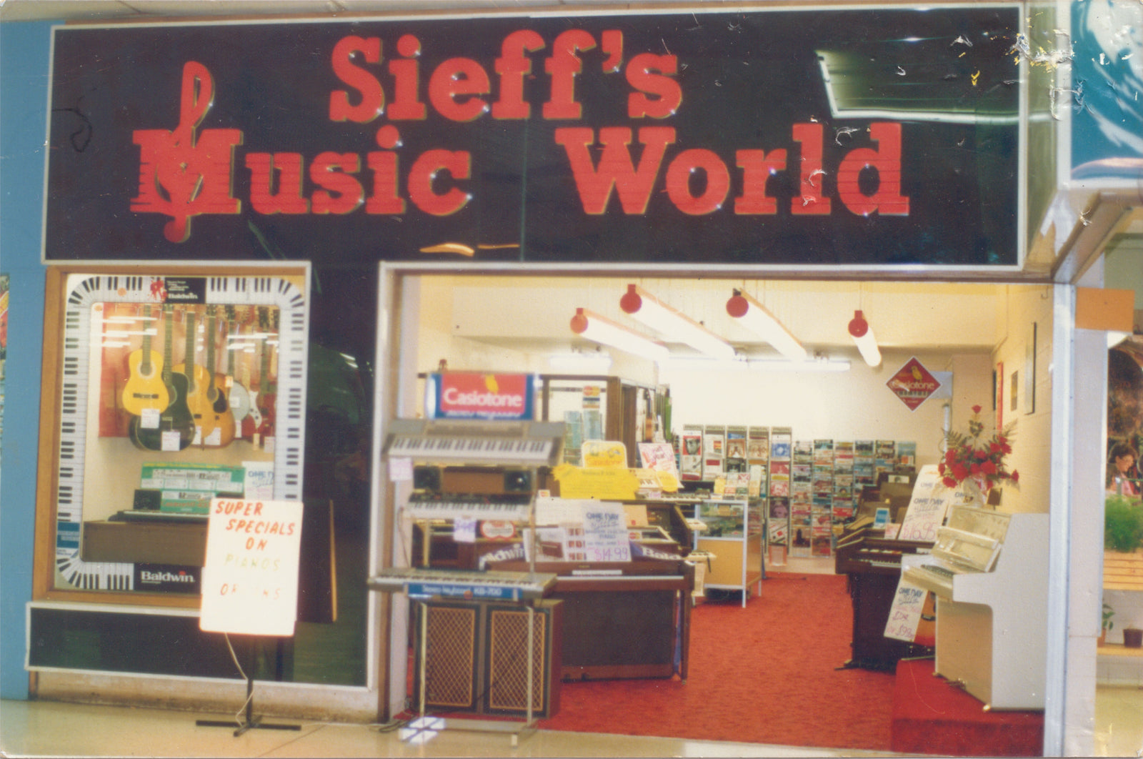Storefront of Sieff's Music World with a large red sign on a black background, glass windows displaying instruments, and an open interior with music equipment and shelves.